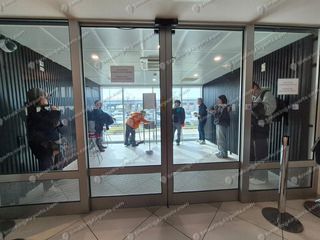 Glass-walled enclosed smoking room at Bari Airport with passengers standing inside near ashtray stand
