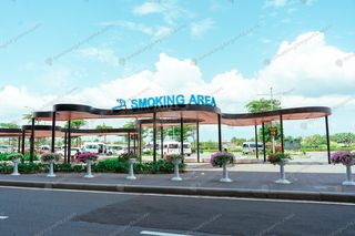 Large open-air smoking canopy with wooden slat roof and flower planters on Cam Ranh Airport forecourt