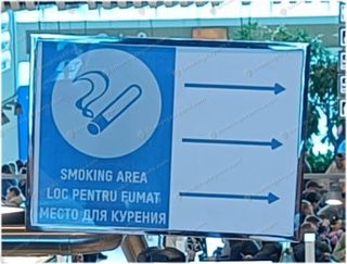 Blue trilingual smoking area sign in Romanian, English and Russian with directional arrows at Chisinau Airport
