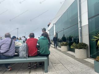 Passengers seated on benches outside Funchal Madeira Airport terminal on an overcast day