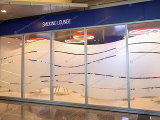 Large glass-fronted smoking lounge with blue sign and colorful pendant lights at Hamad Airport