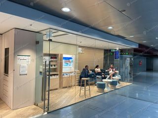 Glass-walled smoke-free lounge cabin near Gate 47 with travelers seated inside on blue stools