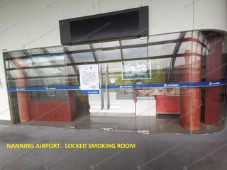 Locked glass-walled smoking cabin inside Nanning Wuxu Airport with official notice on door